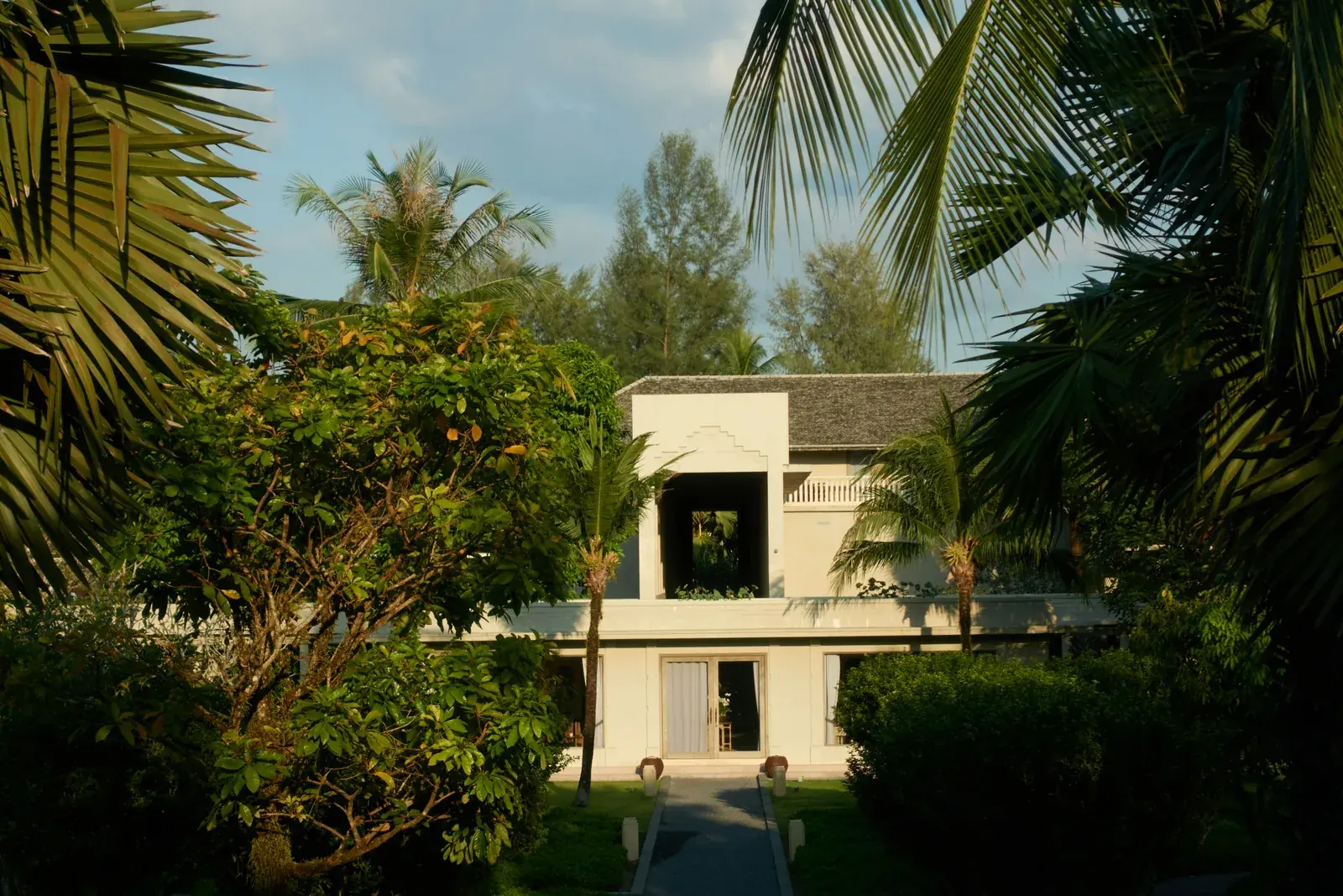 A white villa set among dense tropical planting at dusk